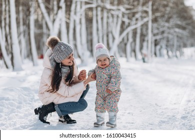 Young mother and her daughter are walking in the winter forest. Snow is falling around.