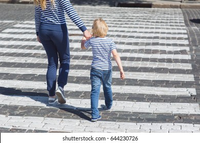 Young Mother And Her Little Child Crossing The Street Holding By The Hand. Boy And Adult Woman Walking On The Crosswalk On The Road With Hard Traffic.