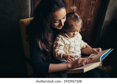 Young mother and her little daughter reading book together sitting in a comfortable chair. - Powered by Shutterstock