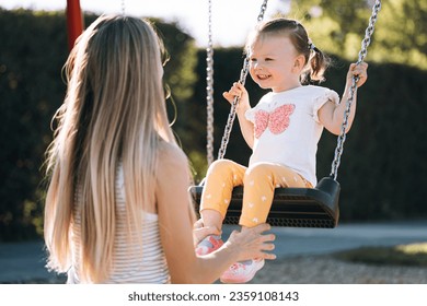 a young mother and her little daughter ride on a swing in the park and are very happy - Powered by Shutterstock