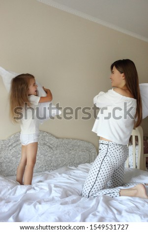 Young mother and her little daughter playing with cushions on bed.