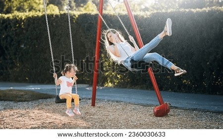 a young mother and her little daughter ride on a swing in the park and are very happy