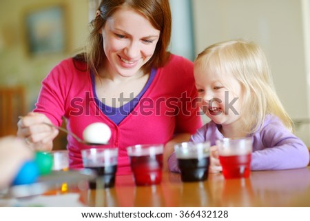 Young mother and her little daughter painting colorful Easter eggs at home