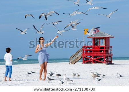 Young mother and her little son feeding seagulls on tropical beach, Florida summer holiday vacation
