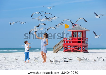 Young mother and her little son feeding seagulls on tropical beach, Florida summer holiday vacation