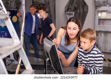 Young mother with her preteen son spending funny time in quest room decorated as lost underground shelter, trying to solve puzzle on computer monitor