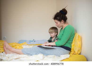 Young Mother And Her Son Toddler Reading Book In A Bed Casual Lifestyle Photo Series In Real Life Interior