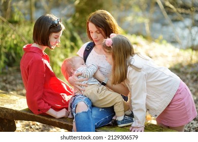 Young Mother And Her Three Kids Having Fun During A Hike In The Woods On Beautiful Sunny Spring Day. Breastfeeding A Baby Outdoors. Active Family Leisure With Kids. Children Exploring Nature.