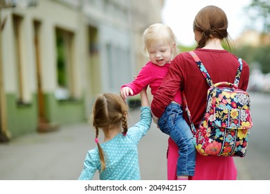 Young mother and her two cute daughters walking down the street on a summer day