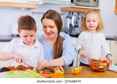 Young Mother And Her Two Kids Making Vegetable Salad