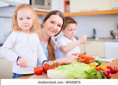 Young Mother And Her Two Kids Making Vegetable Salad