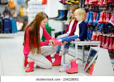 Young mother and her two little girls choosing and trying on new rain boots in a supermarket