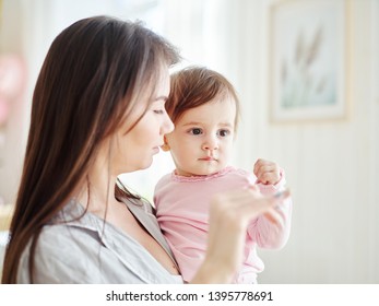 Young Mother Holding Baby Daughter In Arms And Teaching Her How To Wave Goodbye 