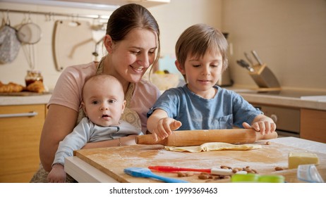 Young Mother Holding Baby Helping Older Son Baking Pizza At Home. Children Cooking With Parents, Little Chef, Family Having Time Together, Domestic Kitchen