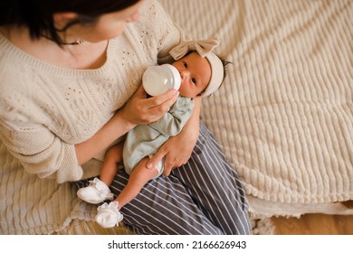 Young Mother Holding Baby On Hands In Bed Feeding With Milk In Plastic Bottle Top View Close Up. Motherhood. Newborn Child With Woman Wake Up And Eating In Morning At Home. Healthy Infant Nutrition.