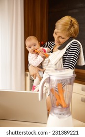 Young mother holding baby, talking on phone, using laptop.