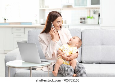 Young Mother Holding Baby While Talking On Phone In Home Office