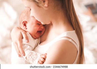 Young mother holding crying baby girl 6-8 months old in room closeup. Motherhood. Maternity. 