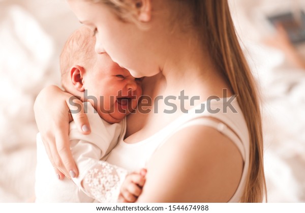 Young mother holding crying baby\
girl 6-8 months old in room closeup. Motherhood. Maternity.\
