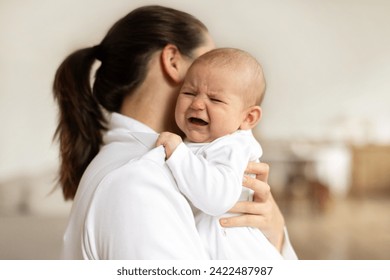 Young mother holding crying newborn baby girl or boy, calming kid, lullying in bedroom interior , focus on baby, free space - Powered by Shutterstock