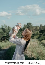 Young Mother Holding Daughter In Her Arms. Happy Harmonic Family Outdoor. Smiling Mommy With Newborn Baby. Woman In Beige And Straw Hat Dress Playing With 4 Month Old Baby. Mountain Landscape 