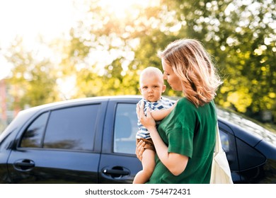 Young Mother Holding Her Little Baby Boy In The Arms Getting Into The Car.