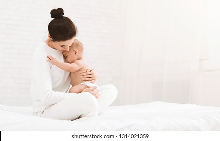 Young mother holding her newborn child, lulling baby in bed, copy space