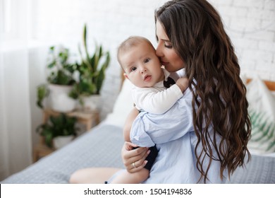 Young Mother Holding Her Newborn Child. Mom Nursing Baby. Woman And New Born Boy Relax. Nursery Interior Family At Home. Portrait Of Happy Mother And Baby