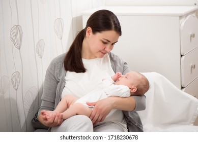 Young Mother Holding Her Newborn Child. Mom Nursing Baby. Woman And New Born Boy Relax In A White Bedroom. Mother Breast Feeding Baby. Family At Home