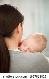 Young Mother Holding Her Newborn Child. Mom Nursing Baby. Woman And New Born Boy Relax In A White Bedroom.