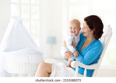 Young Mother Holding Her Newborn Child. Mom Nursing Baby. Woman And New Born Boy In White Bedroom With Rocking Chair And Blue Crib. Nursery Interior. Mother Playing With Laughing Kid. Family At Home