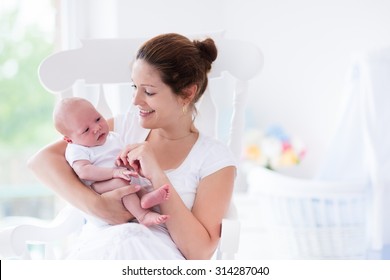 Young mother holding her newborn child. Mom nursing baby. Woman and new born boy relax in a white bedroom with rocking chair and blue crib. Nursery interior. Mother breast feeding baby. Family at home - Shutterstock ID 314287040