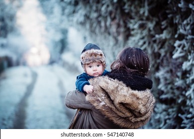 Young Mother Holding Her Newborn Baby With Cap With Ear Flaps. Mother And New Born Boy Having Good Time In The Park In Winter. Baby Boy Is Looking At The Camera. Color Toned Image.