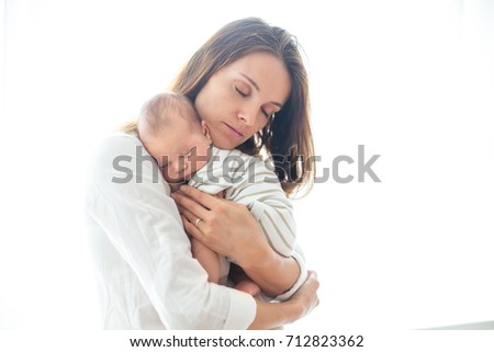 Young mother, holding her newborn baby boy at home in living room, back lit