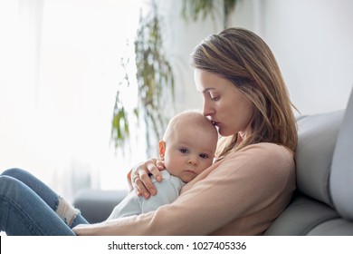 Young Mother, Holding Her Sick Toddler Boy, Hugging Him At Home, Sunny Living Room