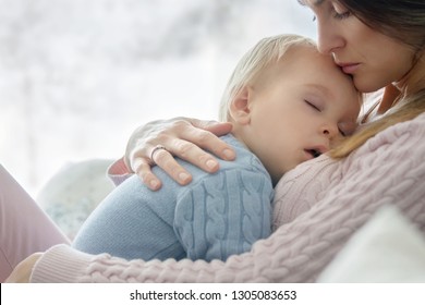 Young Mother, Holding Her Sick Toddler Boy, Hugging Him At Home, Sunny Living Room