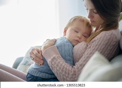 Young mother, holding her sick toddler boy, hugging him at home, sunny living room - Powered by Shutterstock