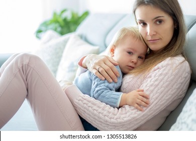 Young Mother, Holding Her Sick Toddler Boy, Hugging Him At Home, Sunny Living Room