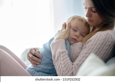 Young Mother, Holding Her Sick Toddler Boy, Hugging Him At Home, Sunny Living Room