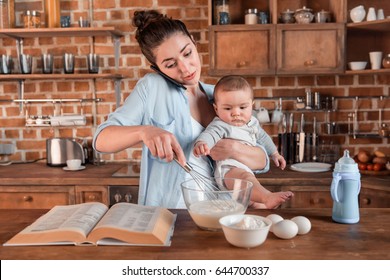 Young mother holding her son, talking on smartphone and mixing a dough at the kitchen. family life and multitasking concept - Shutterstock ID 644700337