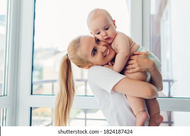 Young Mother Holding And Hugging Newborn Baby Son At Home. Family Relaxing On Balcony. Infant Wearing Diaper