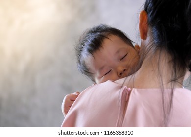 Young Mother Holding Sweet Baby Boy  And Singing A lullabies for Her Son To Sleep, On Concrete Wall Loft Style Background.