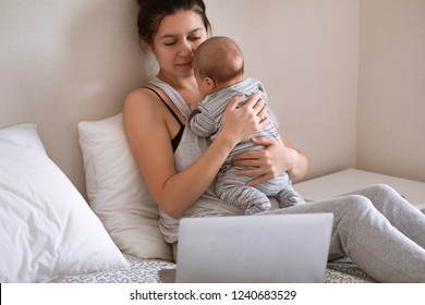 Young Mother In Home Office With Laptop And Her Newborn Baby. Online Treatment And Consultation With A Doctor Concept