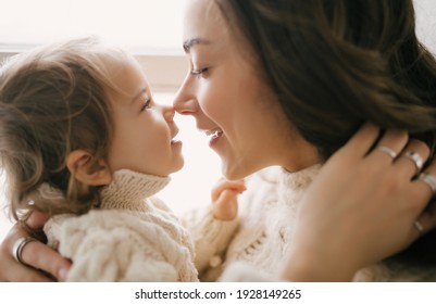 Young mother hugging her little daughter, they sitting near window and smiling.  - Shutterstock ID 1928149265