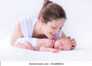 Young Mother Hugging Her Newborn Child. Mom Nursing Baby. Woman And New Born Boy Relax In A White Bedroom. Family At Home. Love, Trust And Tenderness Concept. Bedding And Textile For Nursery.