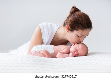 Young Mother Hugging Her Newborn Child. Mom Nursing Baby. Woman And New Born Boy Relax In A White Bedroom. Family At Home. Love, Trust And Tenderness Concept. Bedding And Textile For Nursery.