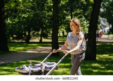 Young Mother Jogging With A Baby Buggy In Summer Park