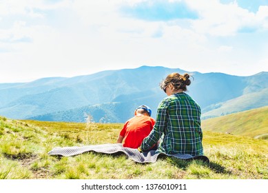 young mother with kid sitting on blanket at mountain peak. beautiful landscape view on background. travel concept. copy space - Shutterstock ID 1376010911