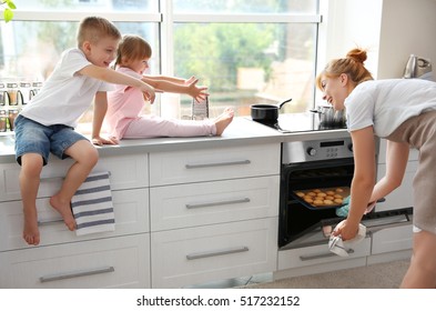 Young Mother And Kids Tasting Biscuits In Kitchen