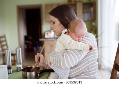 Young Mother In Kitchen Holding Baby Son, Cooking